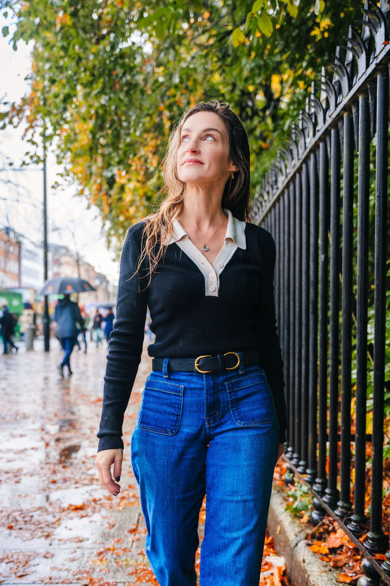 Person in dark sweater and jeans walks along iron fence during autumn with fallen leaves on ground. professional headshots dublin photograph