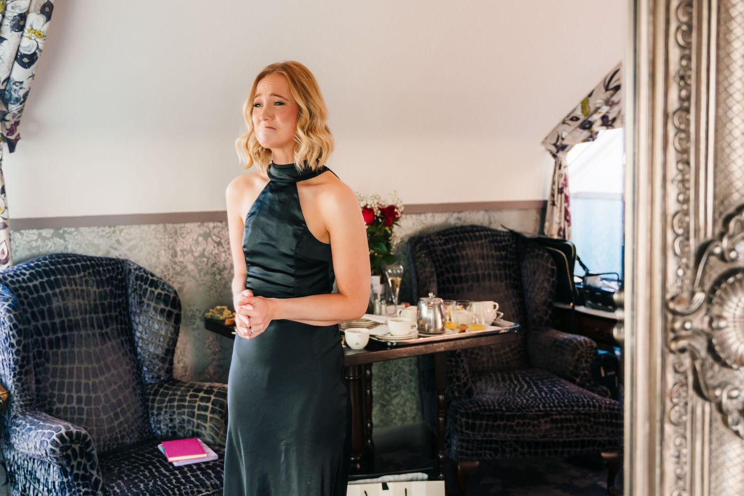 Woman in elegant dark green halter dress stands beside vintage sofa with ornate mirror in background. Wedding photographer dublin
