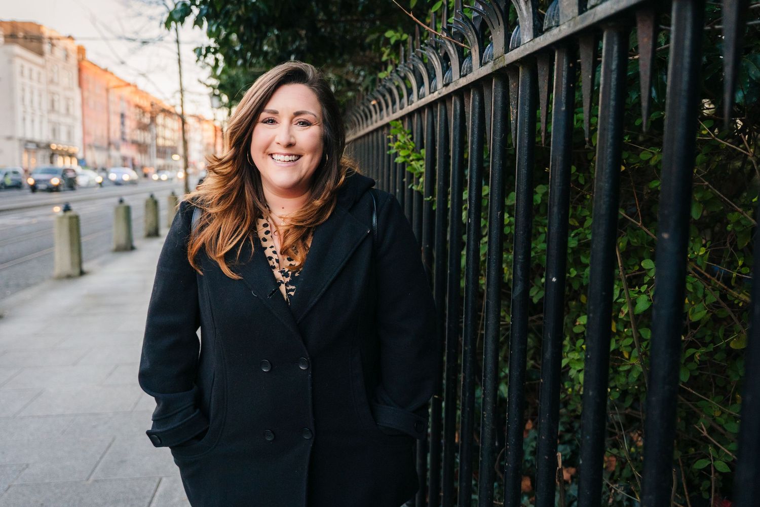Person standing by black iron fence with urban architecture in background. family PHOTOGRAPHER Dublin