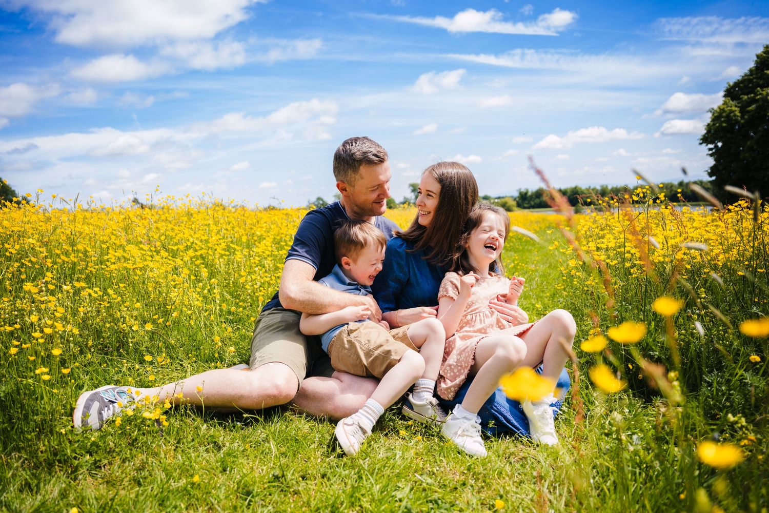A family sits together in a vibrant yellow wildflower meadow on a sunny summer day. Family photographer dublin