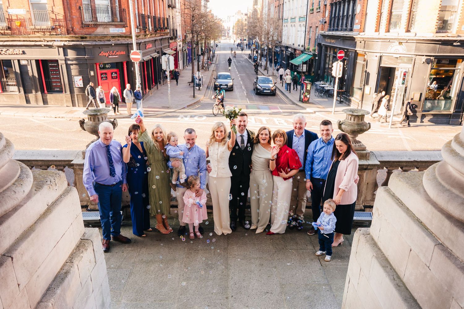Wedding group photo taken on city steps with historic buildings in background. City Hall Dublin wedding photogrAPher
