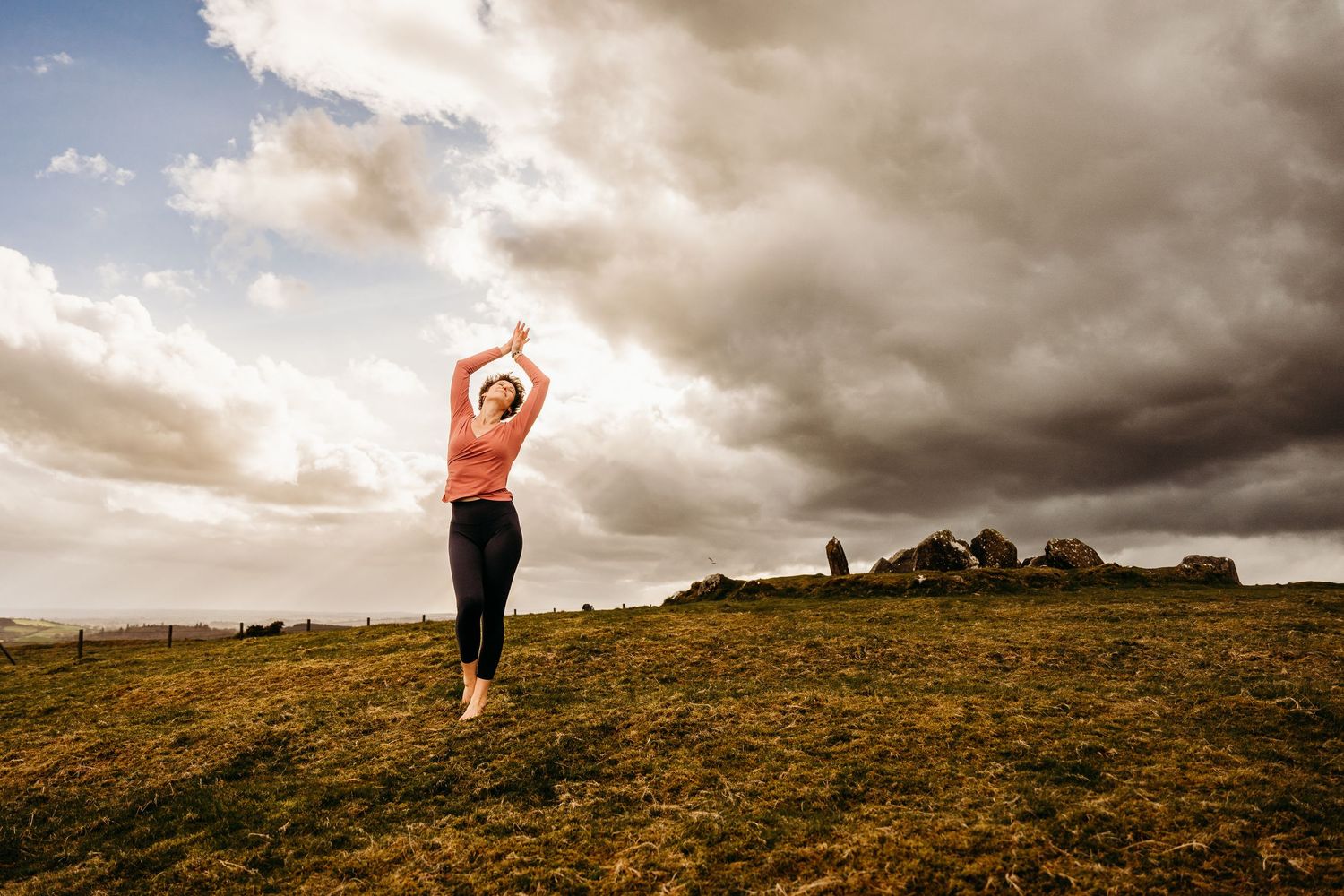 A silhouette stands against dramatic clouds on a grassy hilltop at sunset, captured in a dynamic panoramic sequence. Portrait PHOTOGRAPHER D