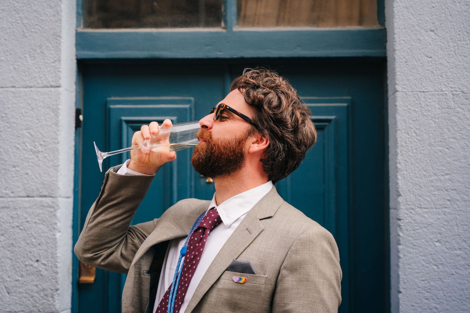 Friends toasting drinks against grey building exterior with blue door. Same sex wedding PHOTOGRAPHER Dublin