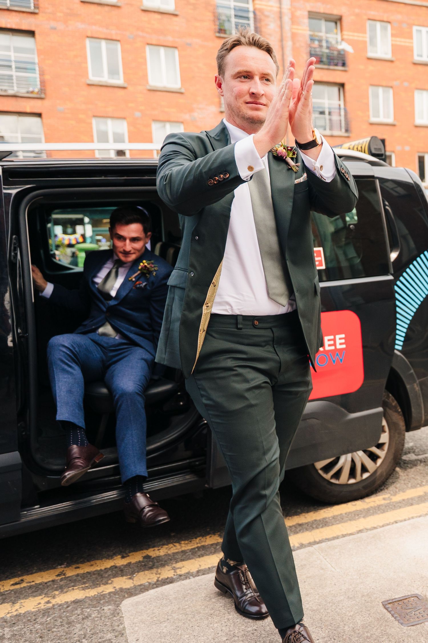 A person in a green suit claps while exiting a taxi cab on an urban street. Same sex wedding PHOTOGRAPHER Dublin