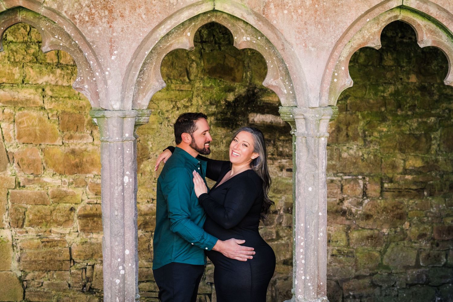 A couple poses together under ornate gothic stone arches in a medieval setting. Family PHOTOGRAPHER Dublin