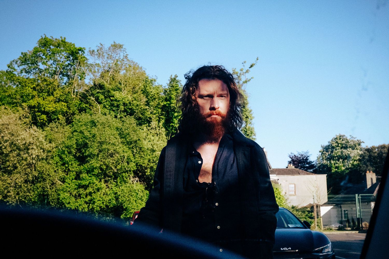 Person with long dark hair wearing black jacket stands against green foliage backdrop. PHOTOGRAPHER Dublin