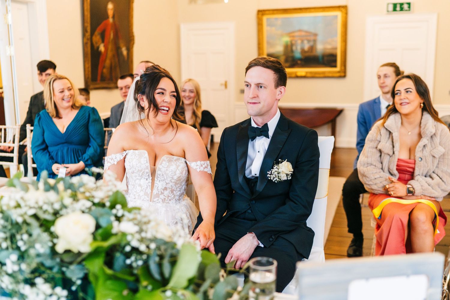 Wedding guests seated in an elegant room with gold-framed artwork and floral centerpieces.  Wedding PHOTOGRAPHER Dublin
