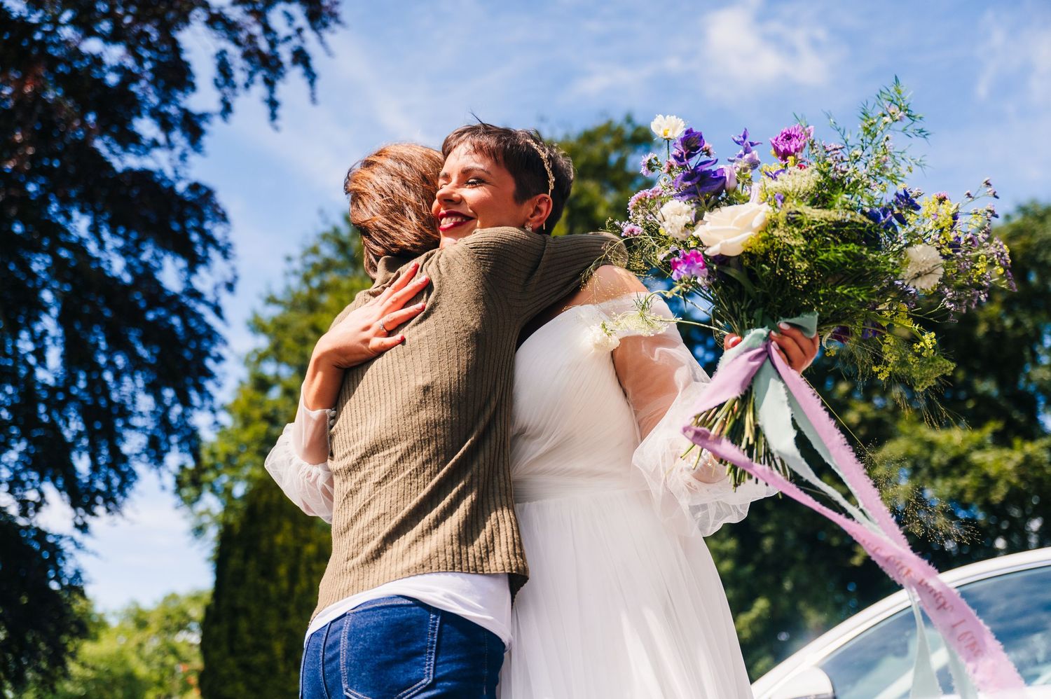 Guest hugs couple in embrace during outdoor wedding reception under blue sky.Millhouse slane wedding photographer dublin