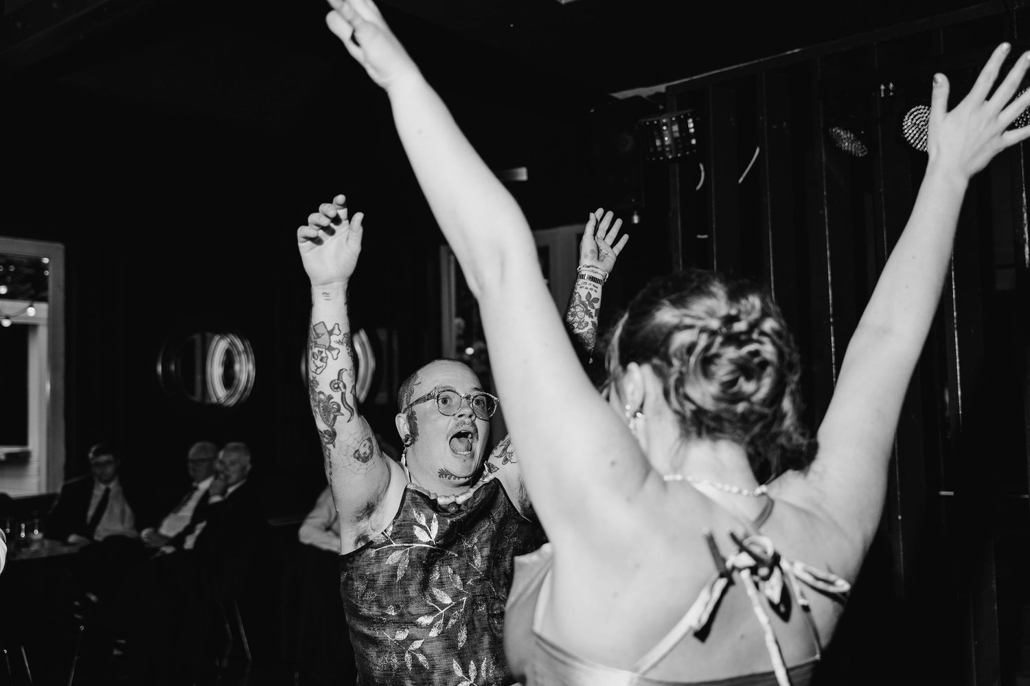 A black and white photograph shows energetic people dancing with their arms raised at what appears to be a party or celebration.Poulaphouca