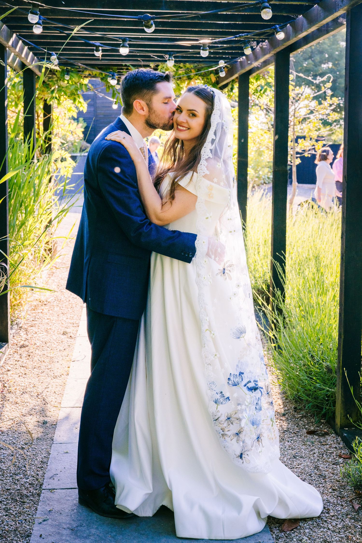 Poulaphouca Wedding photographer wicklowA romantic wedding moment under a pergola decorated with string lights in an outdoor garden setting.