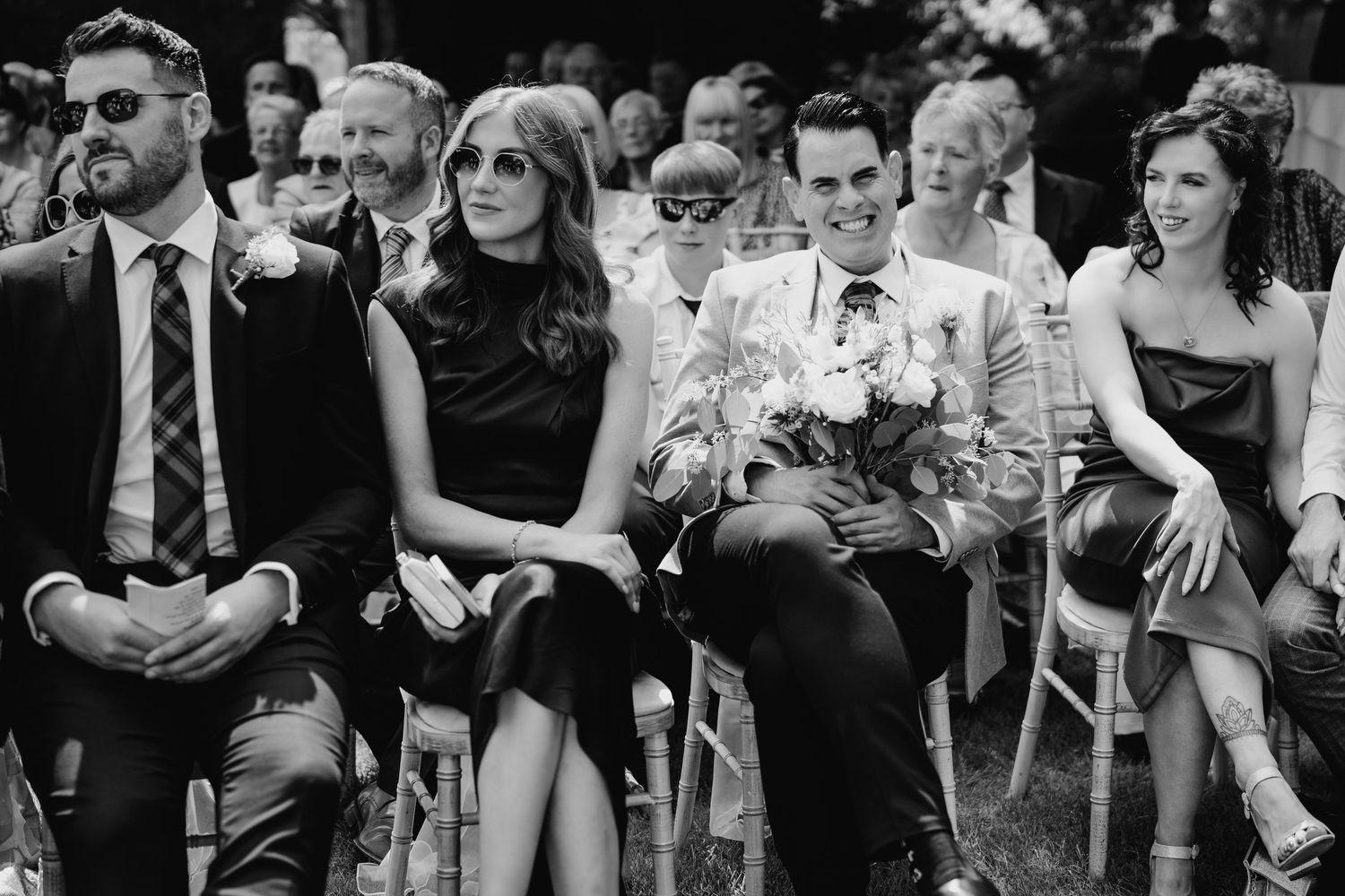Guests seated at formal event in black and white photo with audience members watching an outdoor ceremony. Portmarnock Hotel Wedding PHOTOGR