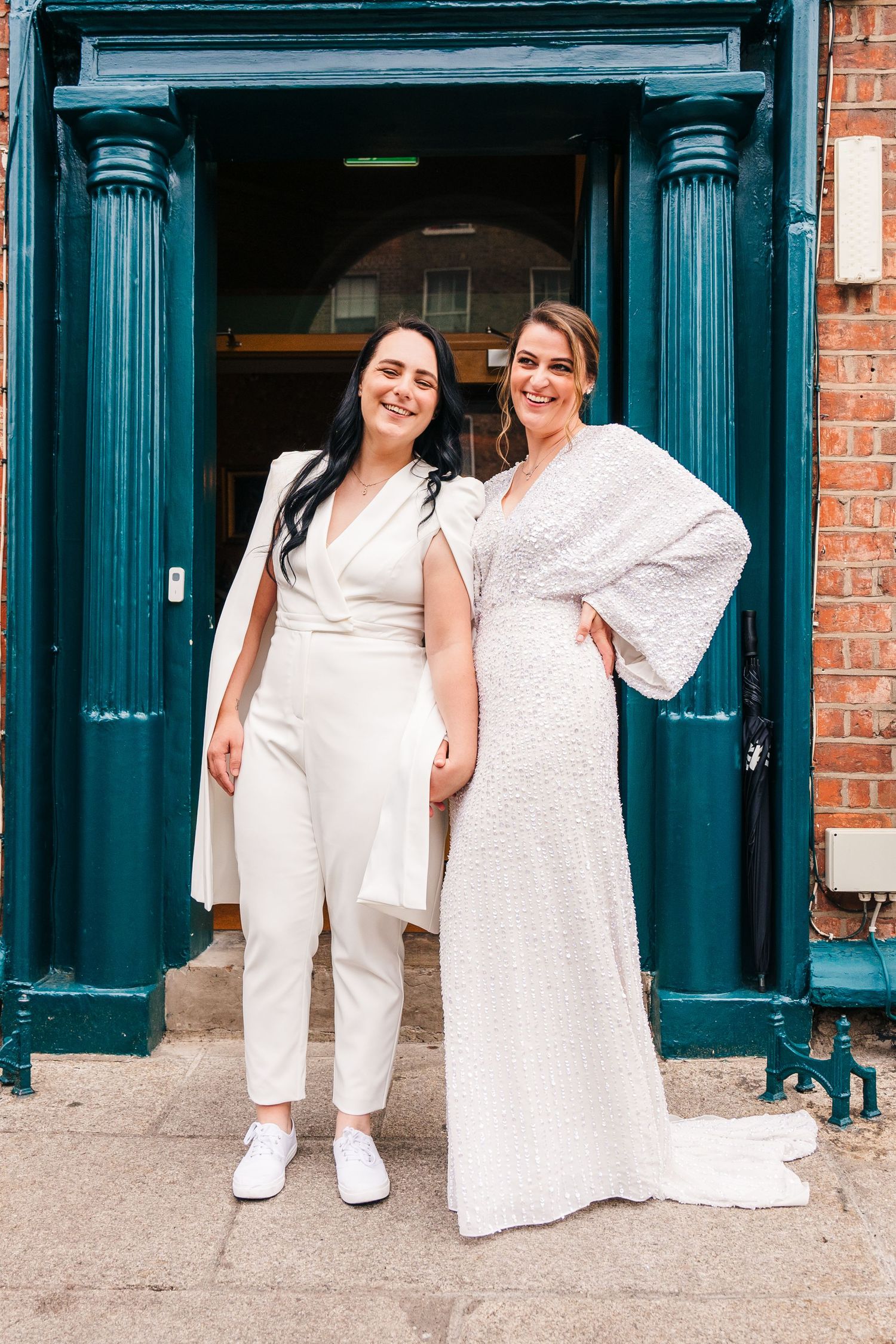 Two people in white formal attire pose in a doorway with teal columns and brick walls. House Dublin Wedding Photographer