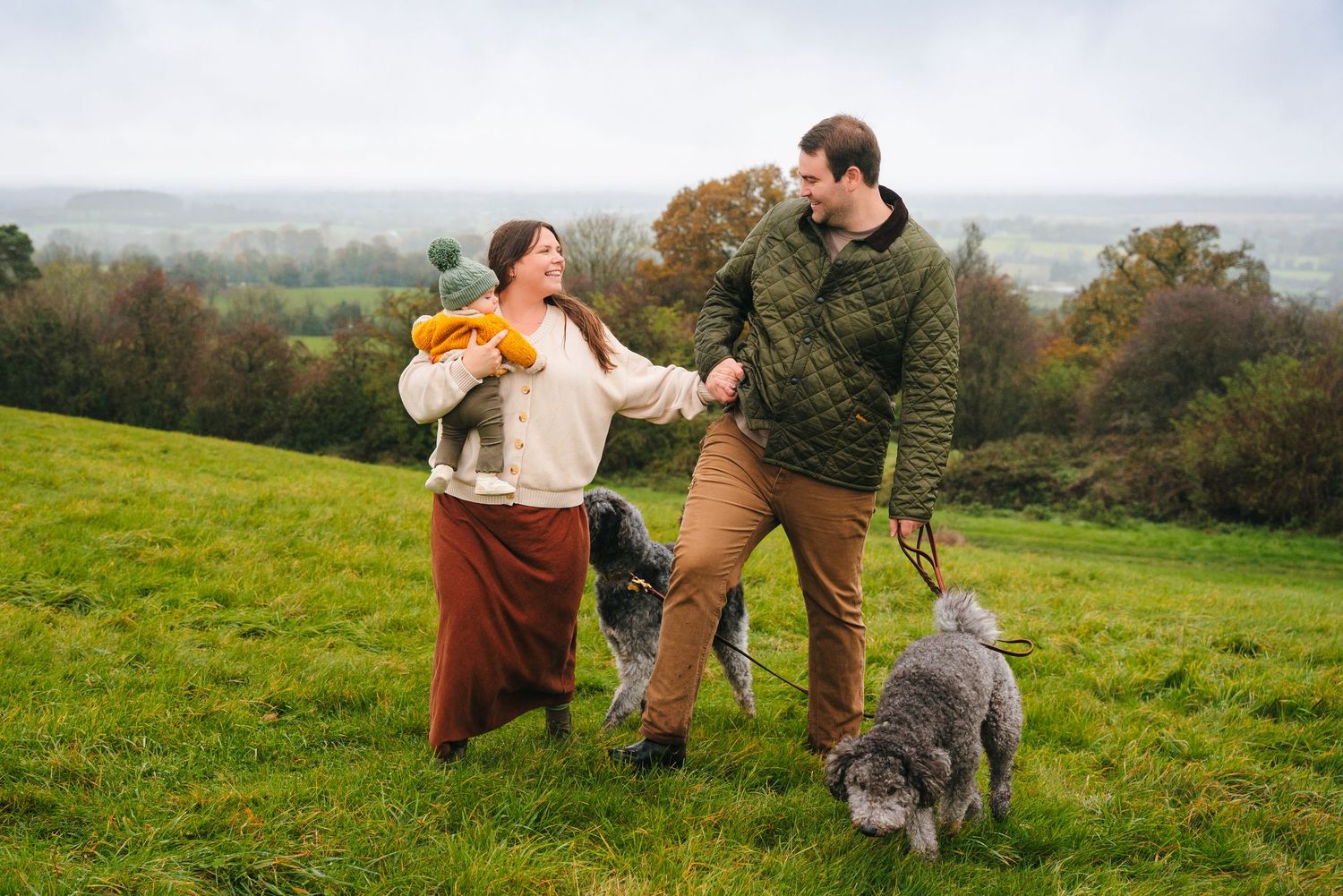 A person walks their dog across a green hillside meadow on an autumn afternoon. Family photographer Dublin