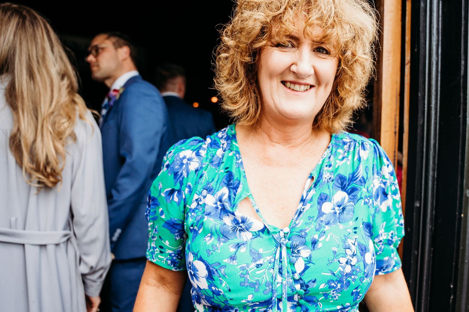 Wedding guest in vibrant blue floral dress smiling at outdoor celebration. Wedding photographer Dublin