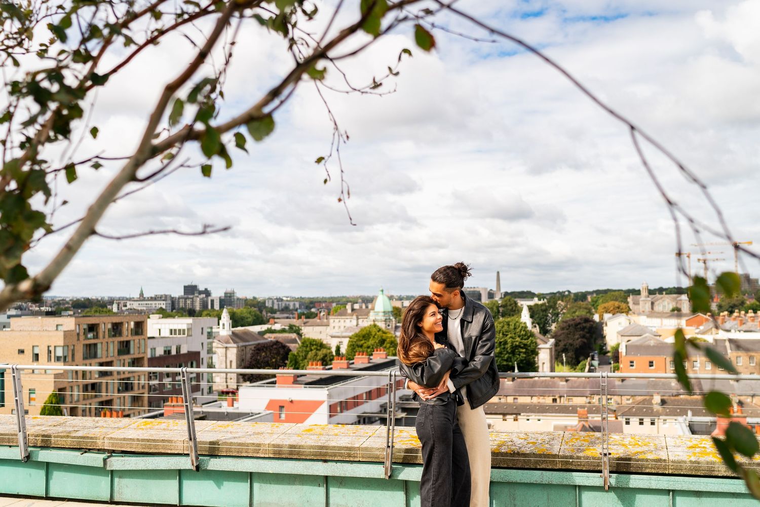 City rooftop view with tree branches framing urban buildings against cloudy sky. Couple's Photoshoot PHOTOGRAPHER Dublin