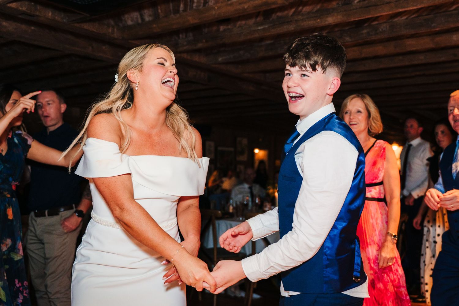 Guests enjoying lively dancing and celebration at wedding reception under wooden beams. The Dean Dublin Wedding Photographer