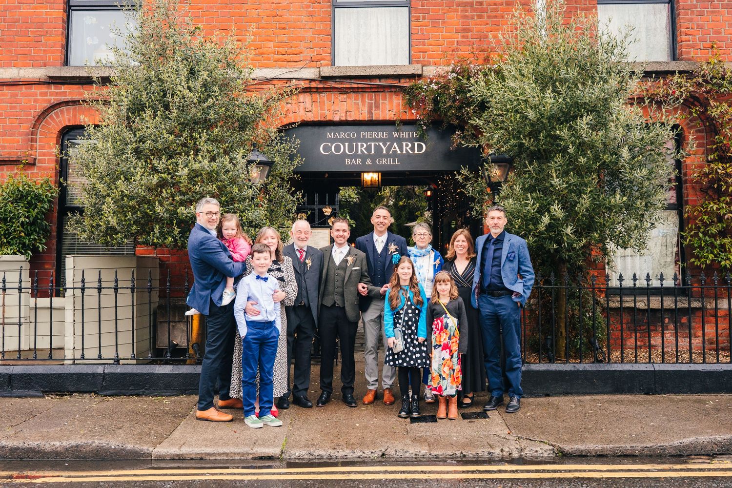 Wedding guests gathered outside a red brick courtyard building entrance for a group photo. Marco Pierre Dublin Wedding Photographer
