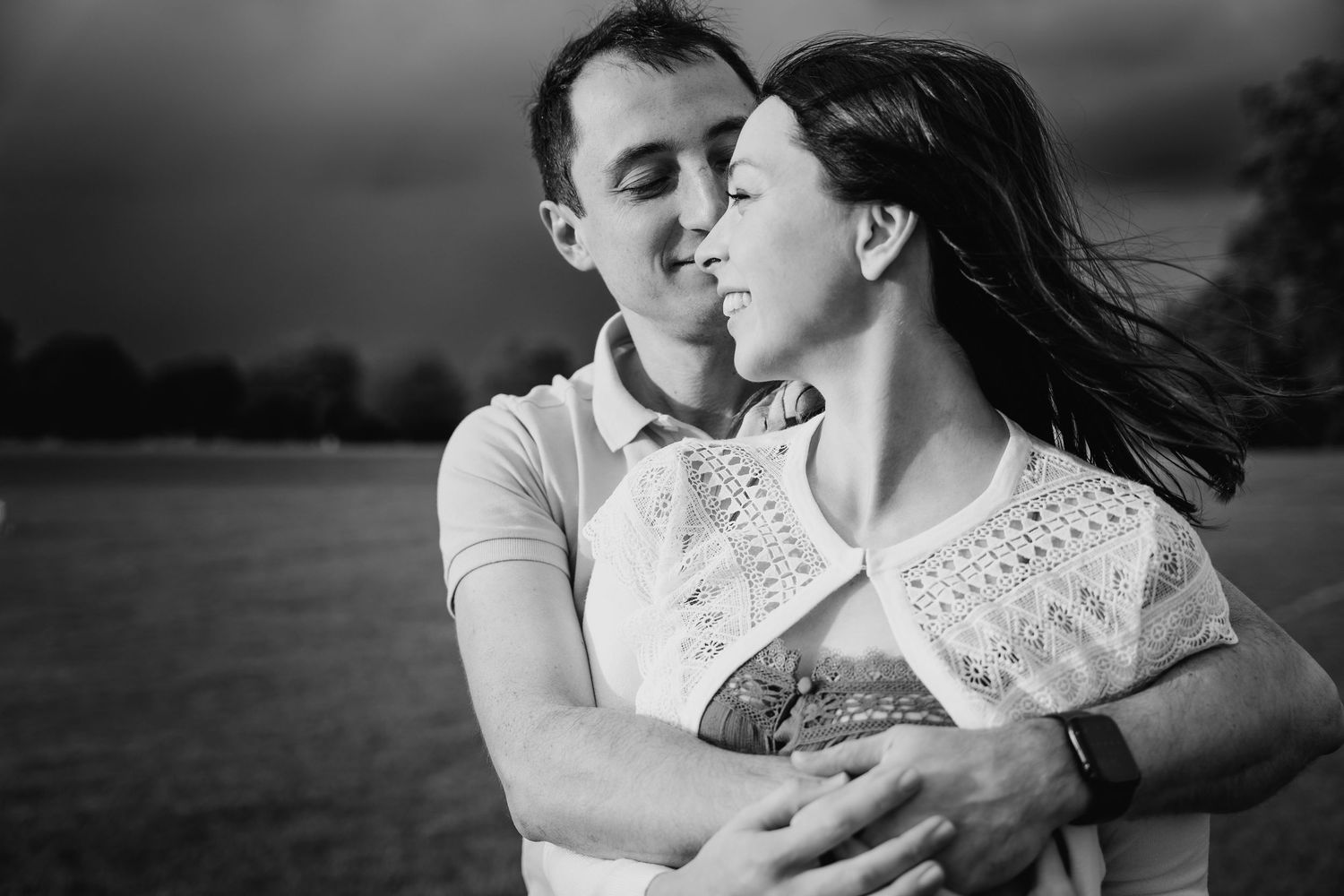 Black and white romantic portrait of a couple embracing in a field with wind-blown hair and white lace clothing. PHOTOGRAPHER Dublin ireland