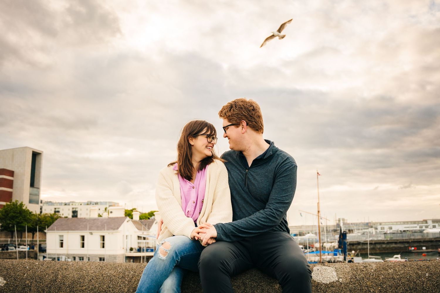A couple shares an intimate moment outdoors while a seagull soars overhead against a cloudy sky. PHOTOGRAPHER Dublin ireland