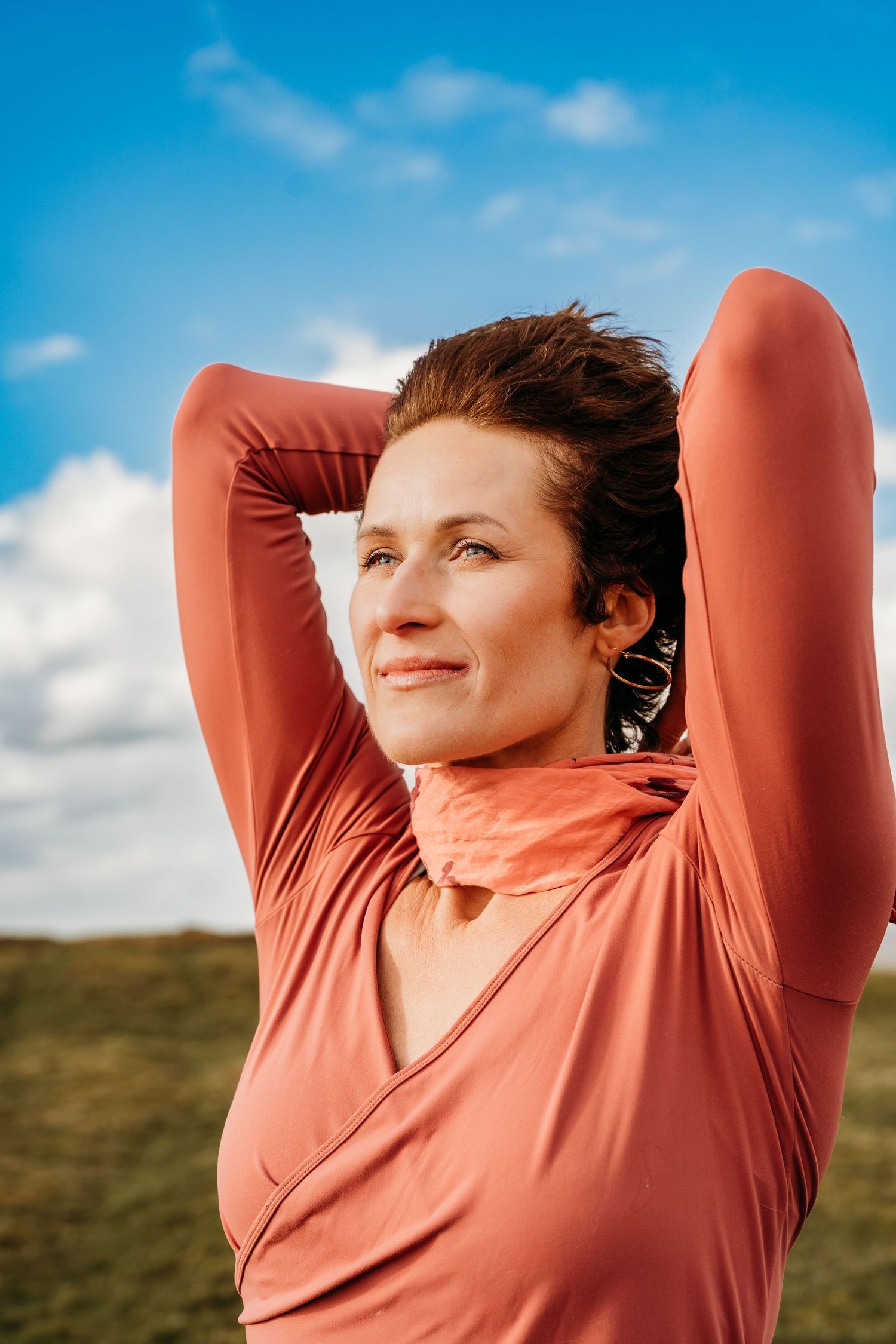 A person in a coral-colored athletic top stretches outdoors against a blue sky with white clouds. PHOTOGRAPHER Dublin ireland