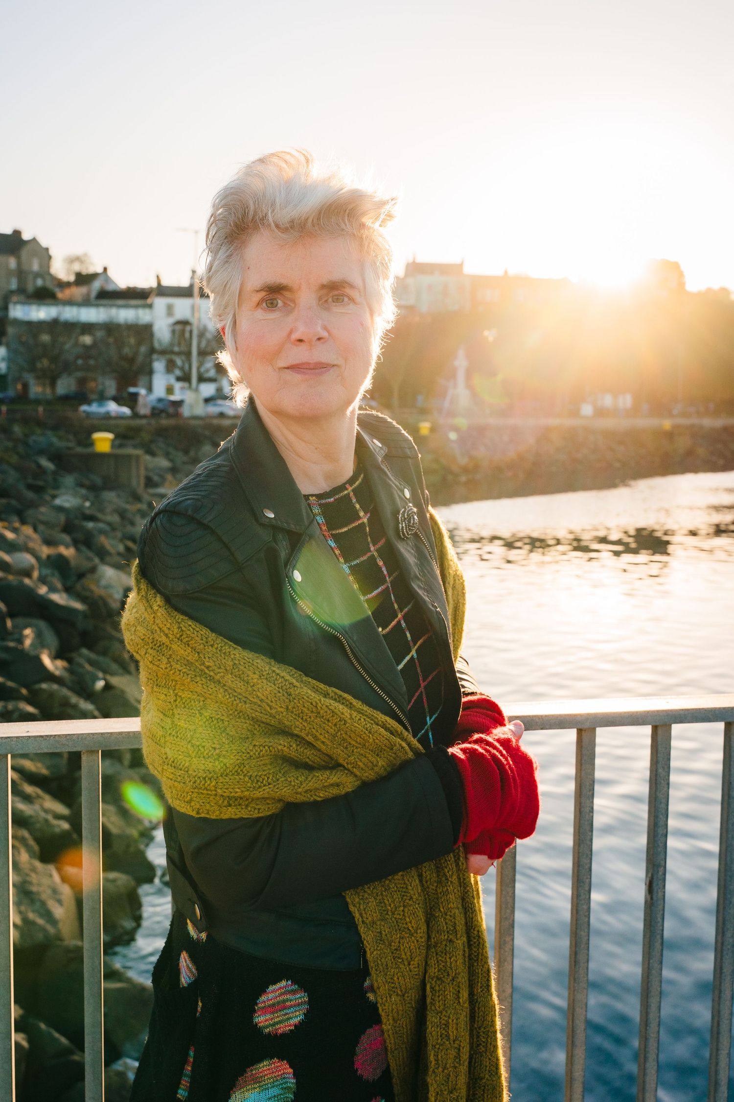 Person in dark coat with mustard scarf poses by waterfront during golden hour. professional headshots branding photographer dublin ireland