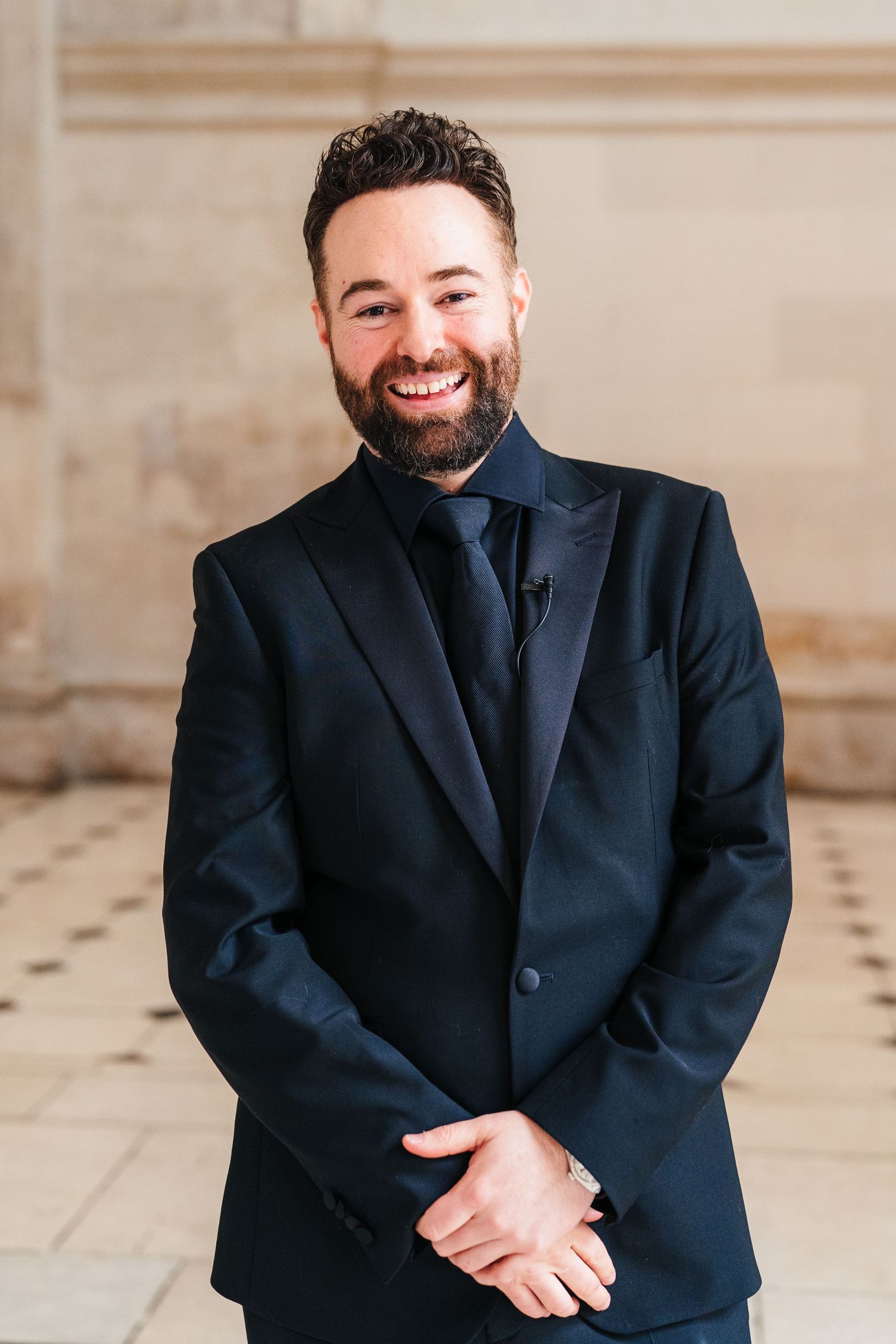 Person in navy suit jacket smiling and posing against neutral background.  city hall dublin wedding photos