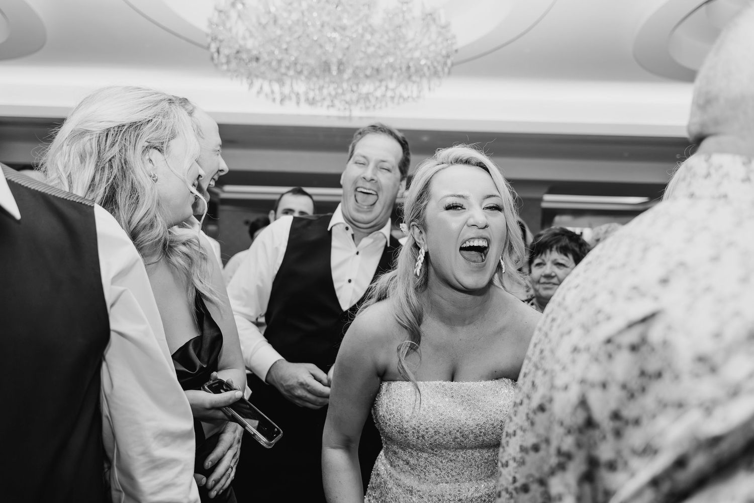 A candid black and white photo capturing joyful laughter and celebration during a wedding reception. Wedding PHOTOGRAPHER Dublin