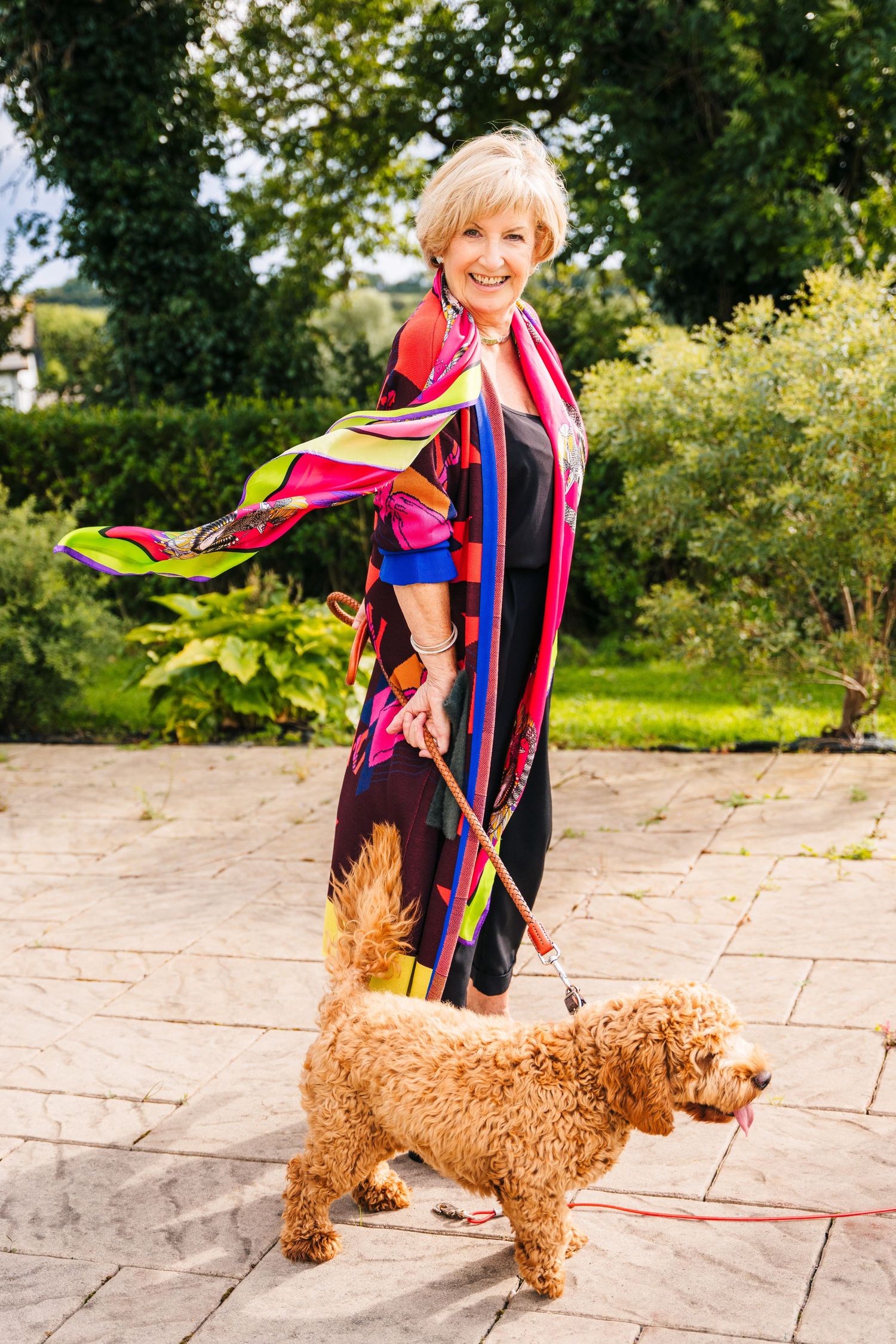 A person in colorful clothing plays with a golden-brown poodle dog on a stone patio surrounded by greenery. PHOTOGRAPHER Dublin ireland
