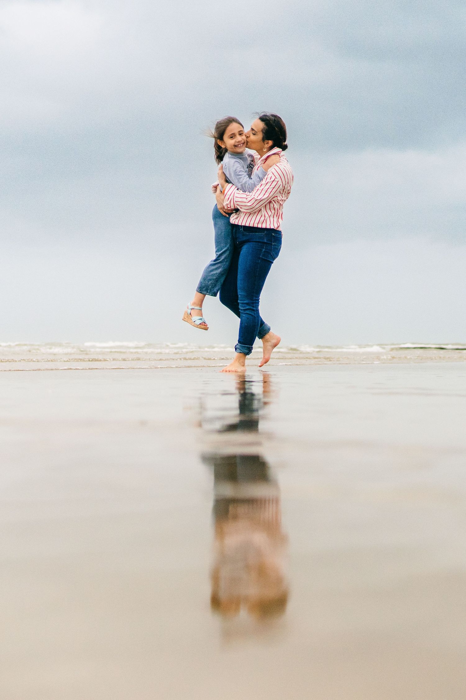 Couple embracing and spinning together on a misty beach with their reflection visible in the wet sand. family PHOTOGRAPHER Dublin
