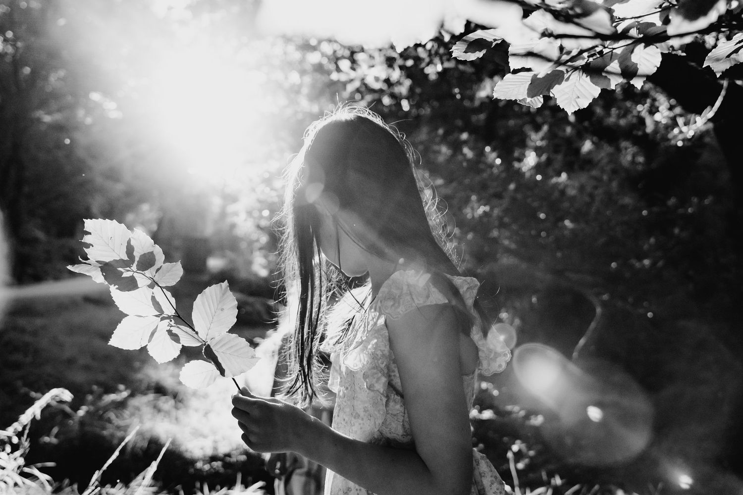 A dreamy black and white photograph showing a silhouette among blossoming flowers at sunset with lens flare effects. family PHOTOGRAPHER Dub
