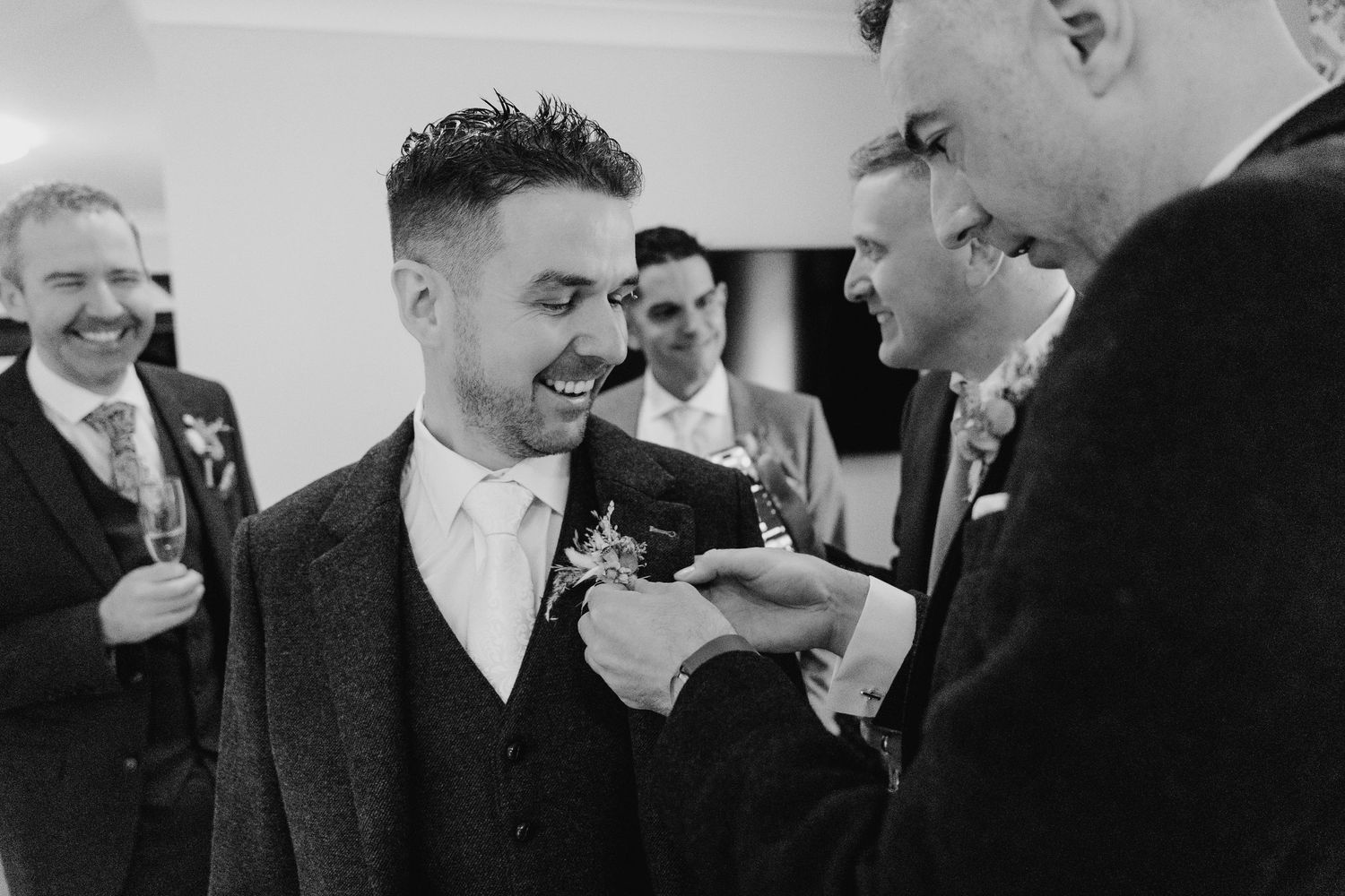 A black and white candid moment captured during wedding preparations with formal attire and boutonnieres.