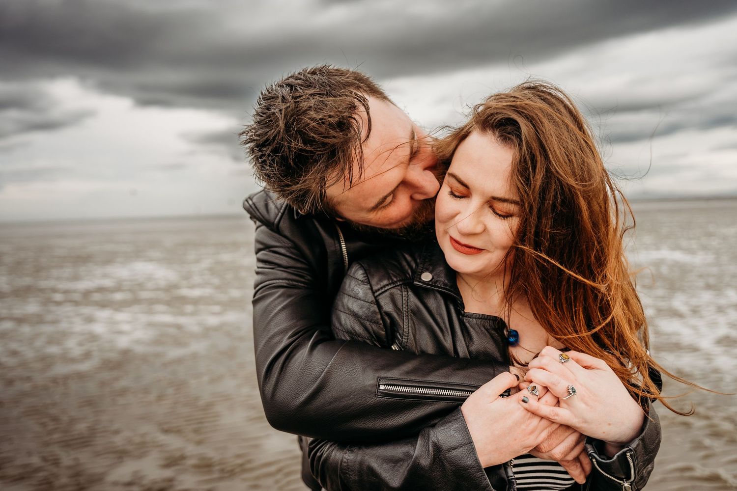 Romantic couple embracing on beach with dramatic cloudy sky in background. engagement PHOTOGRAPHER Dublin