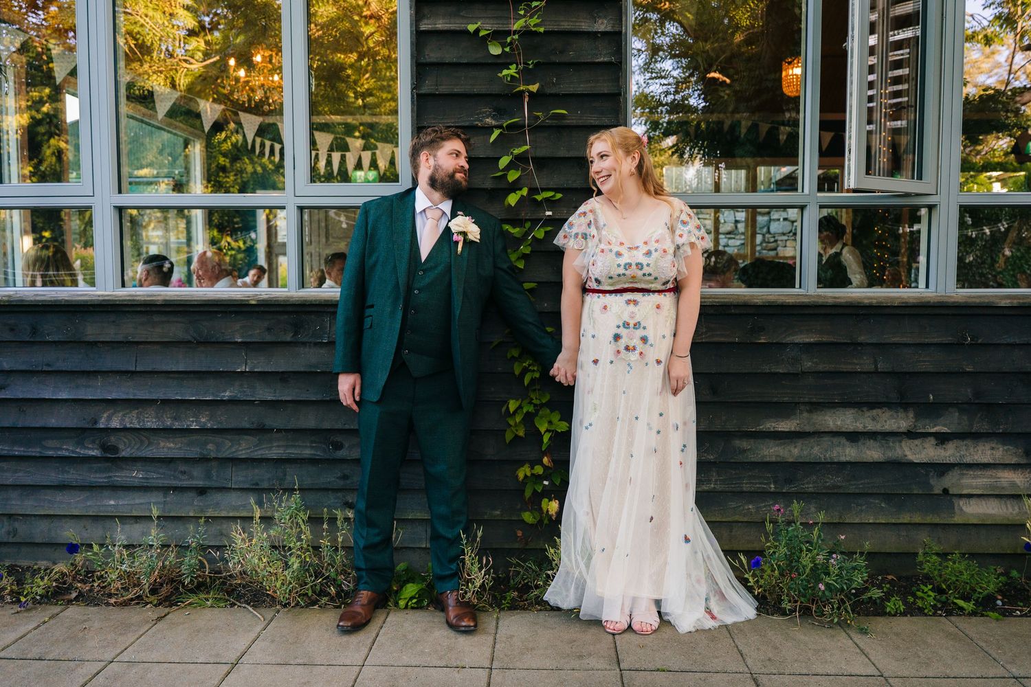 Couple posed outside wooden building with autumn foliage and large windows. . Village Barn Tyrrellspass wedding photographer Ireland