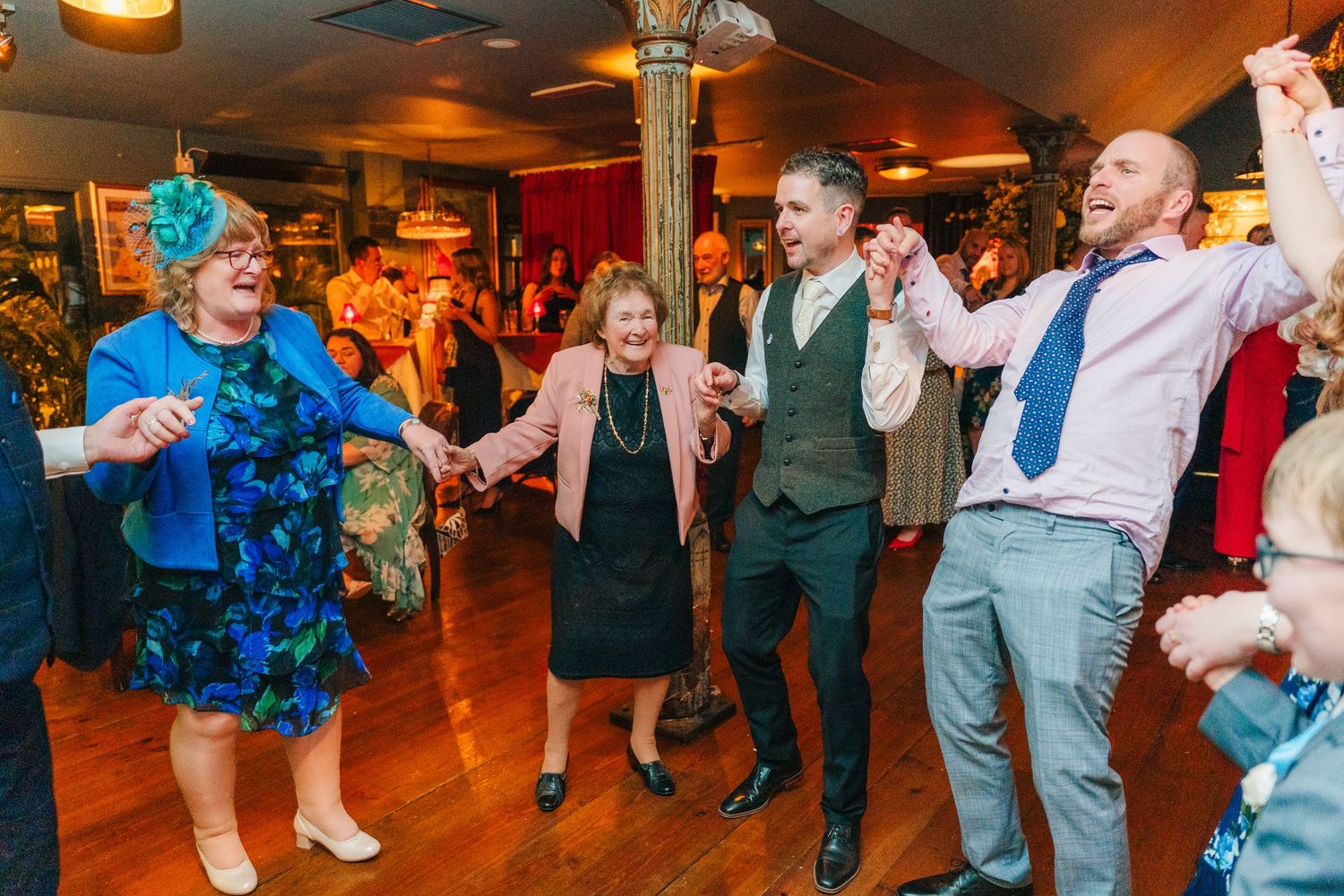 Wedding reception guests dance energetically on a warmly lit dance floor.