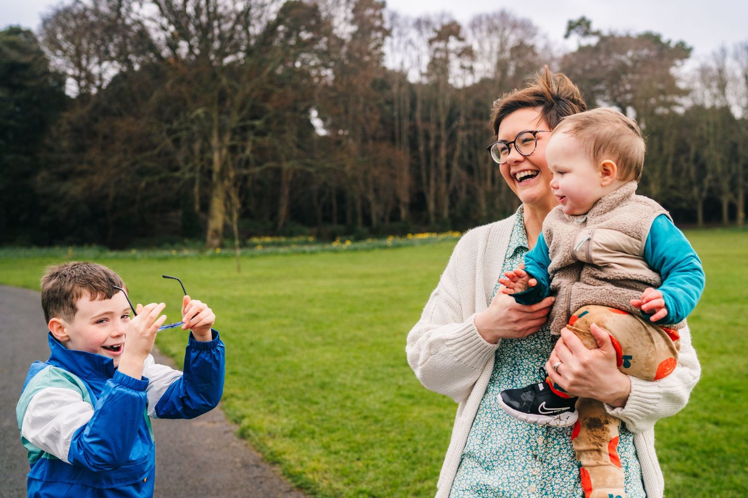 Four candid shots at a park showing playful interaction between two people on a green field with trees in background. Family photographer Du
