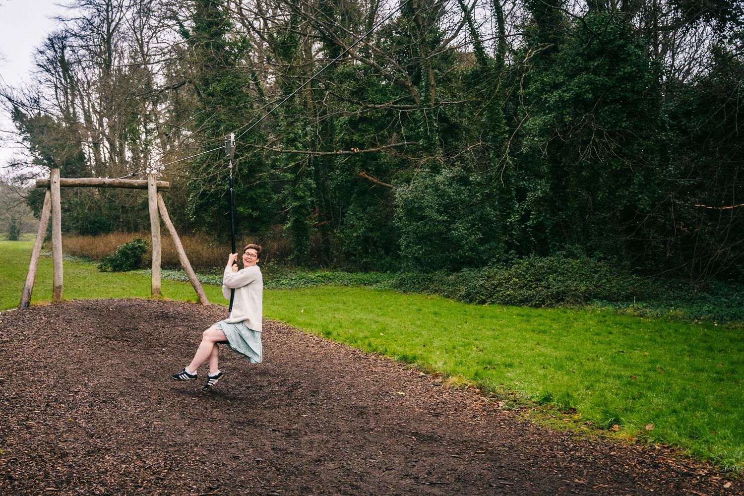 Family photographer Dublin Ireland  Someone enjoys swinging at a playground surrounded by green trees and grass.