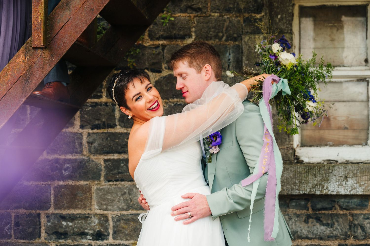 Happy couple embraces and laughs during wedding celebration against rustic stone wall backdrop.Millhouse slane wedding photographer dublin