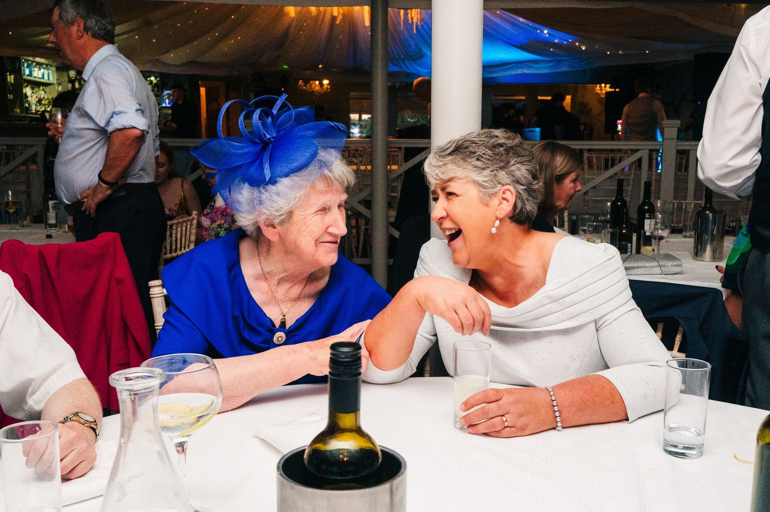 Millhouse slane wedding photographer dublin Wedding reception guests socialize and share laughs around dining tables in evening lighting.
