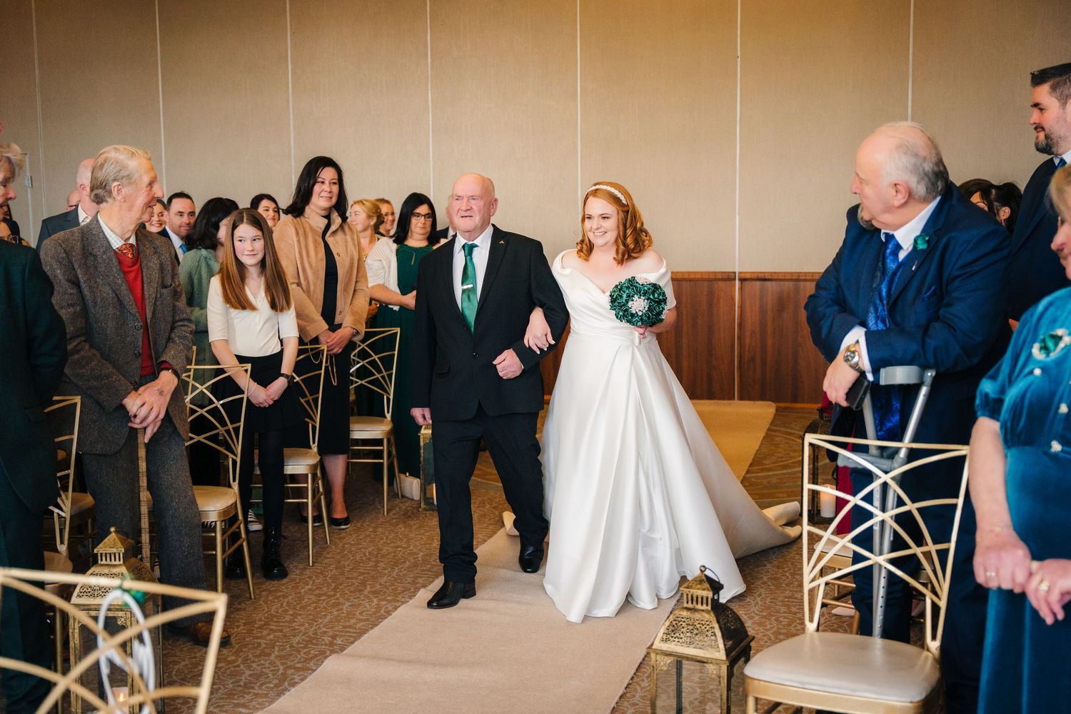 Wedding ceremony taking place in an elegant indoor venue with guests seated in white chairs.  Wedding PHOTOGRAPHER Trim Castle