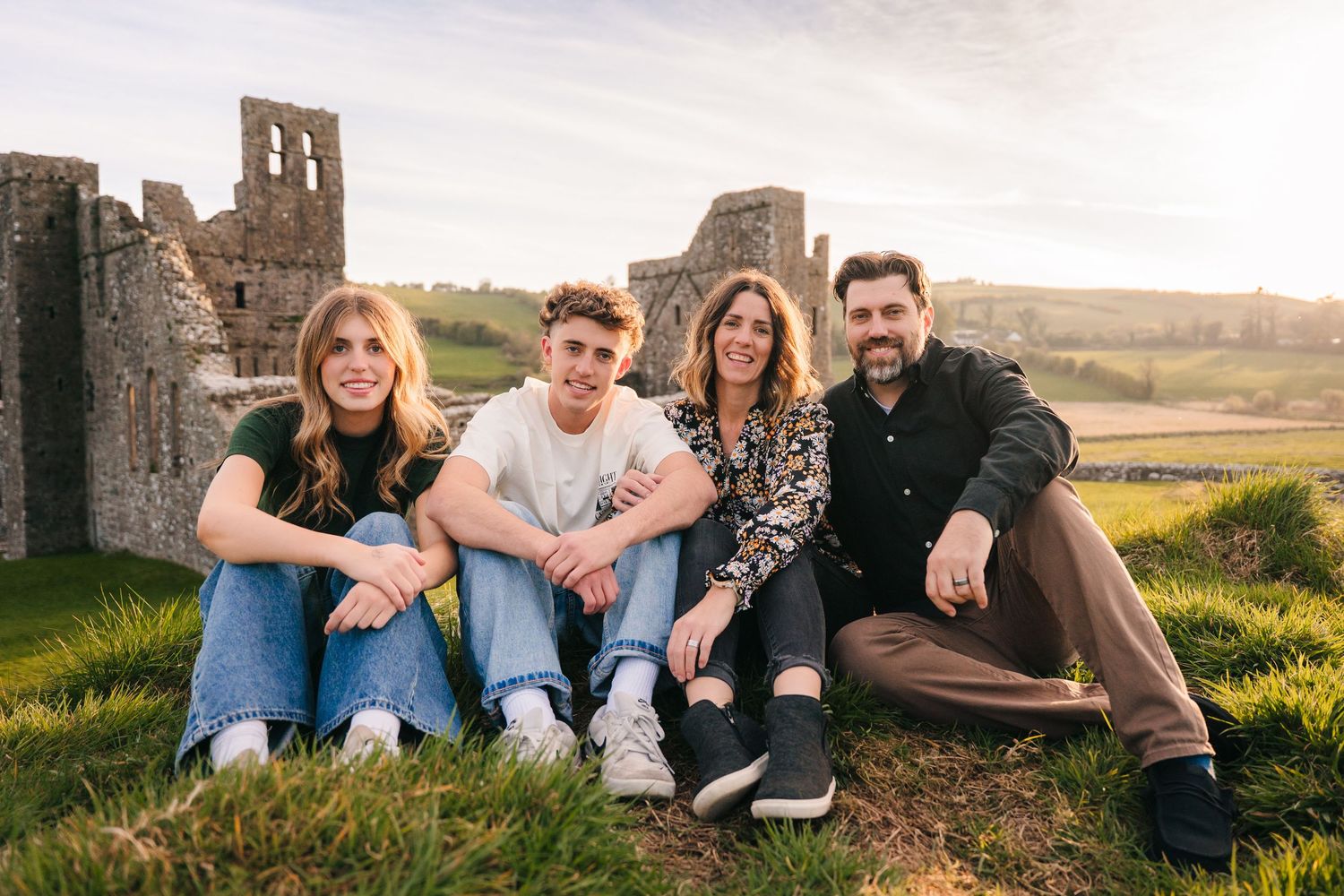 Group of friends lounging on grass near historic ruins during golden hour. Photographer Ireland dublin