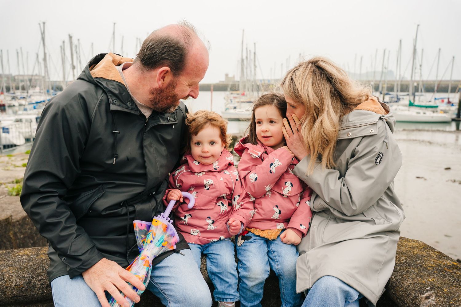 A family sits together on rocks near a marina enjoying a casual outdoor moment. PHOTOGRAPHER Dublin