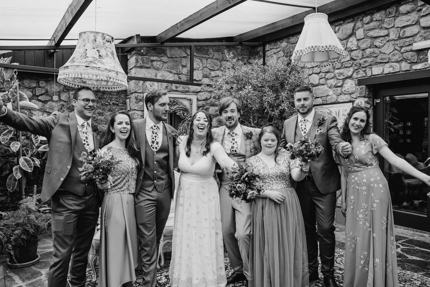 Wedding party poses together in formal attire against rustic stone wall backdrop. Wedding photographer Dublin