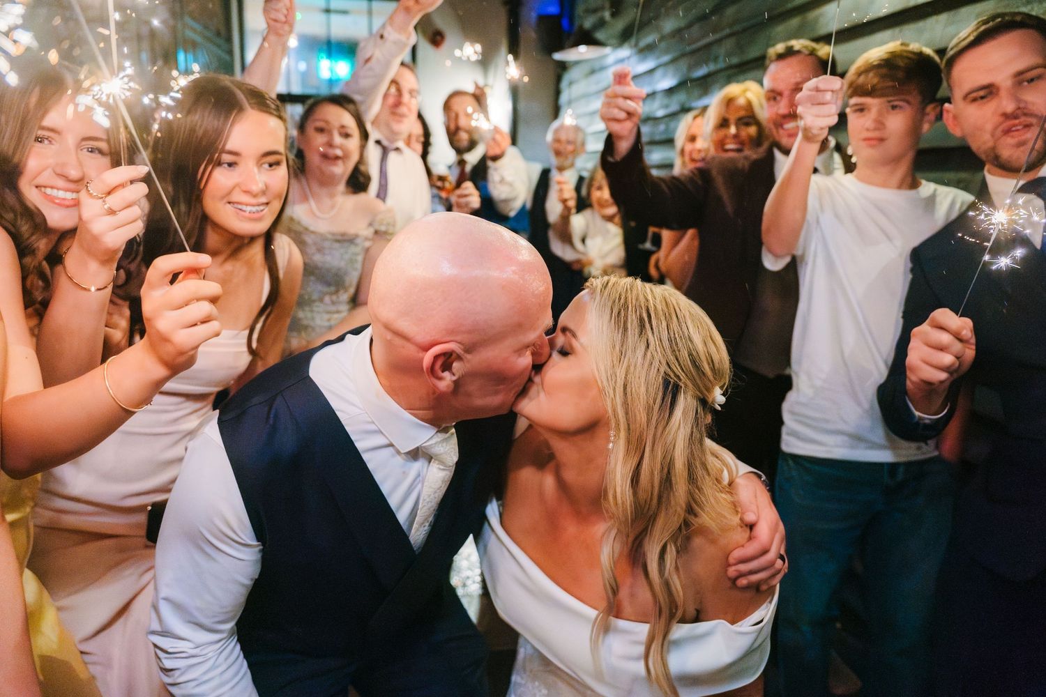 A crowded dance floor at a wedding reception with guests wearing white shirts and dancing together under dim lighting. Wedding photographer