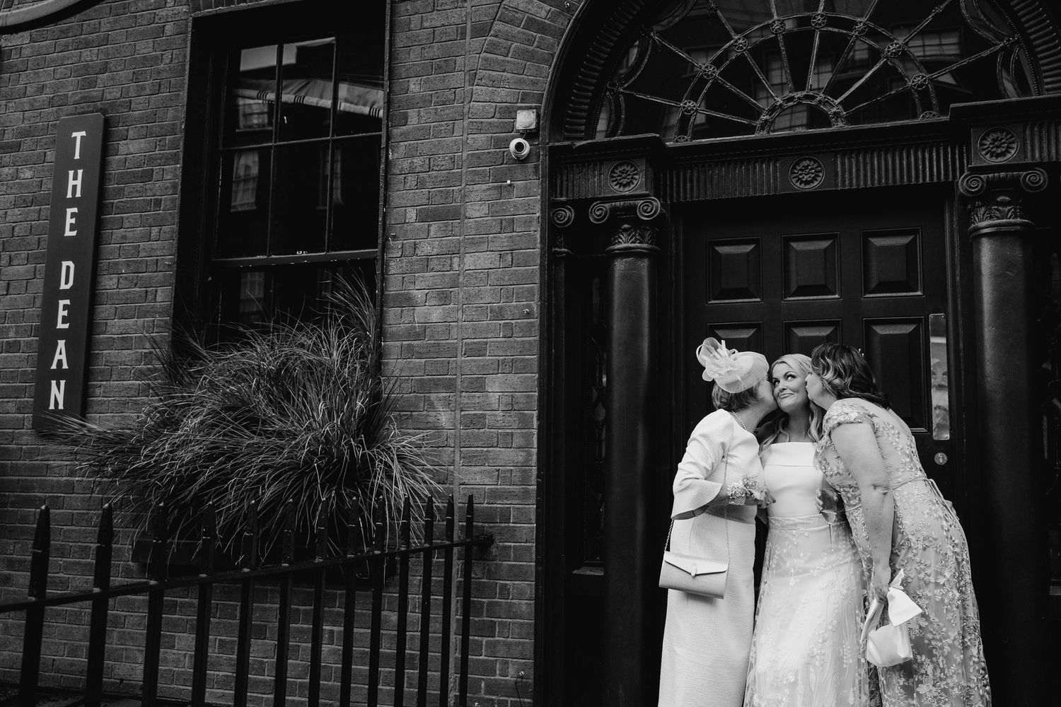 Black and white image of a romantic moment at a brick wall facade during a wedding celebration. The Dean Dublin Wedding Photographer