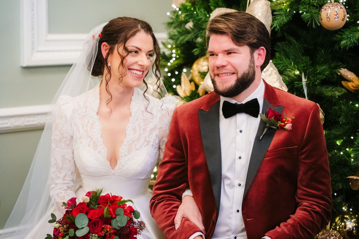 A romantic winter wedding moment with a couple in formal attire against a backdrop of Christmas decorations and greenery. Stephens green clu