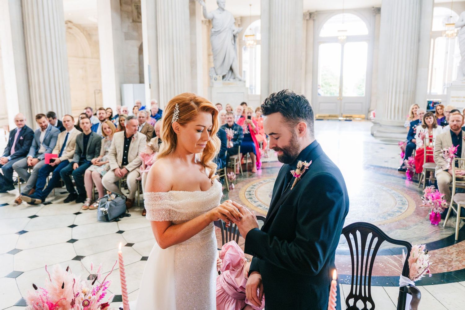 Elegant wedding ceremony takes place in a grand columned hall with pink floral decorations.  city hall dublin wedding photos