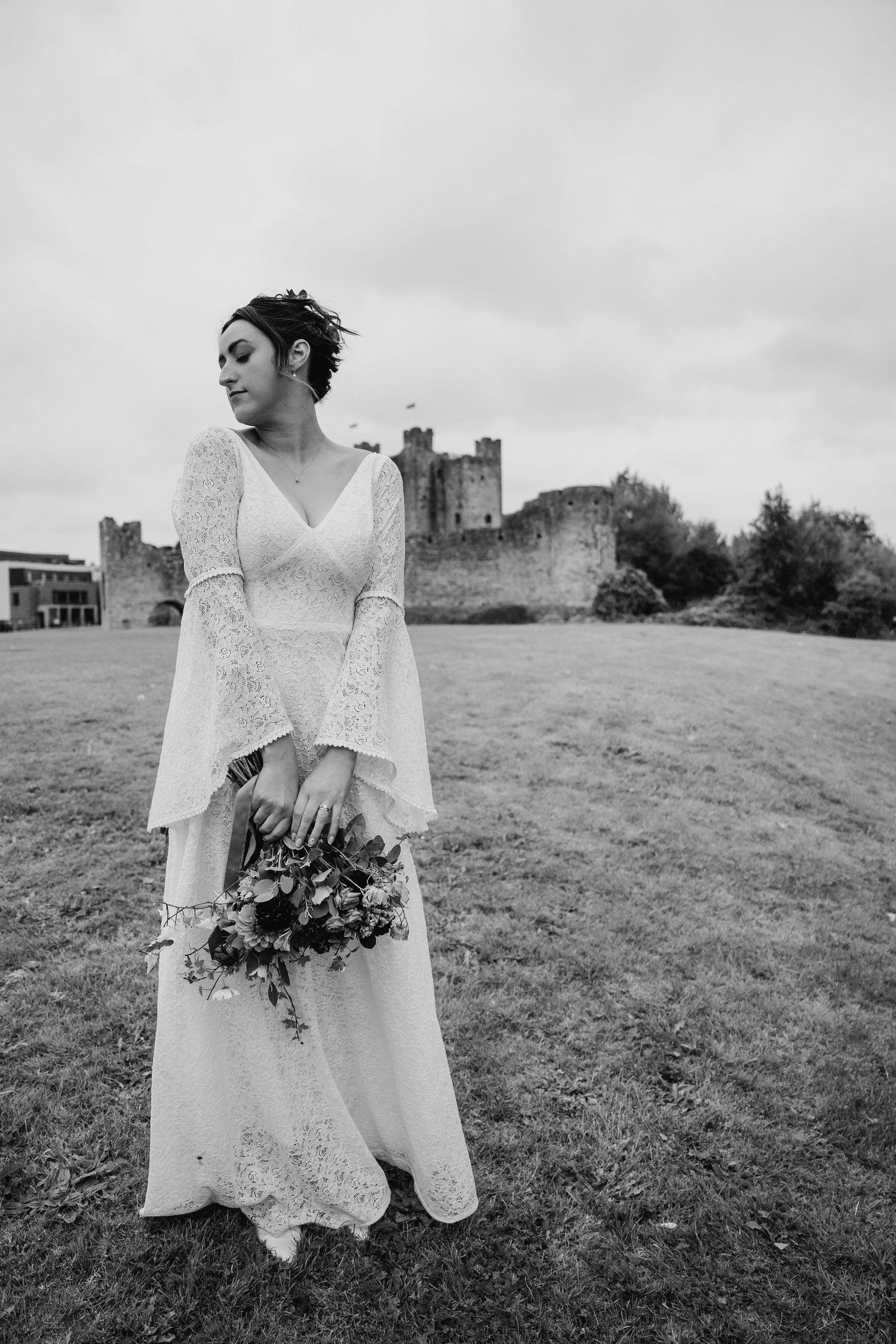 Bride in boho lace dress holding bouquet with castle ruins in background.Wedding Photography Trim Castle Ireland