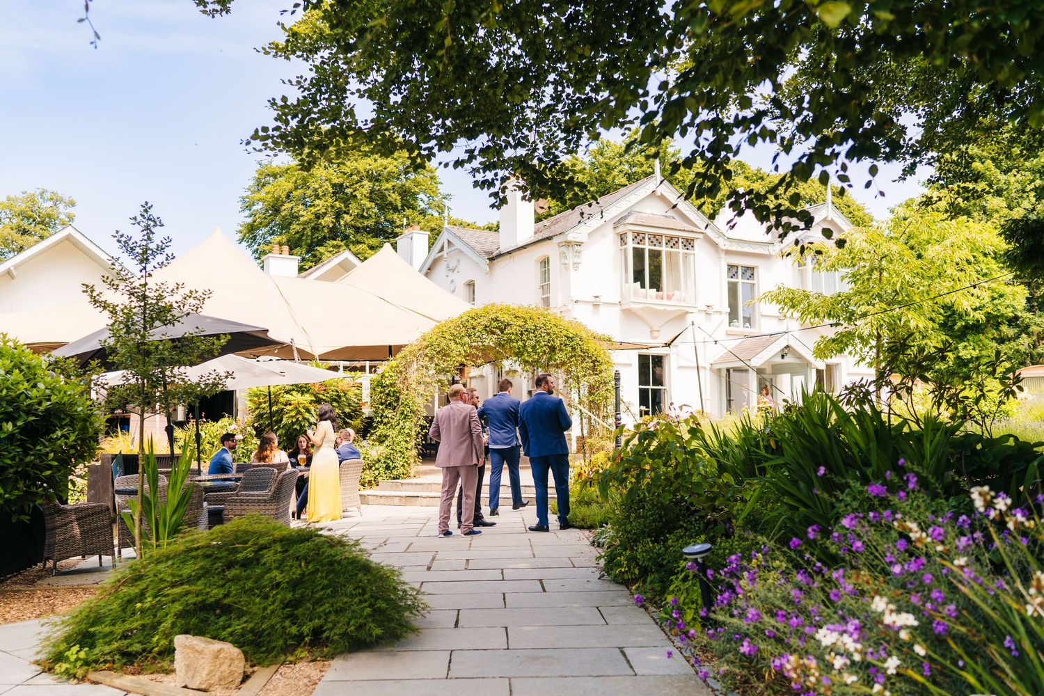 Poulaphouca Wedding photographer wickloElegantly landscaped garden path leading to a classic white manor house with guests gathered outside.