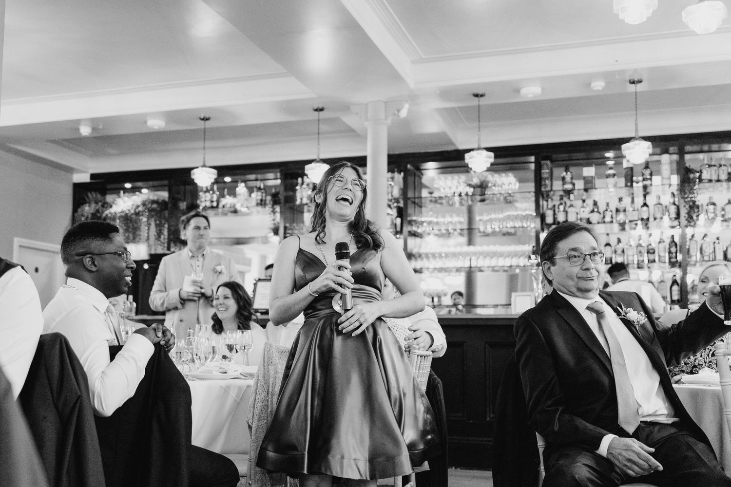 Wedding guests celebrate with raised arms during a lively reception at a venue with a bar backdrop. PHOTOGRAPHER Dublin Ireland Wedding
