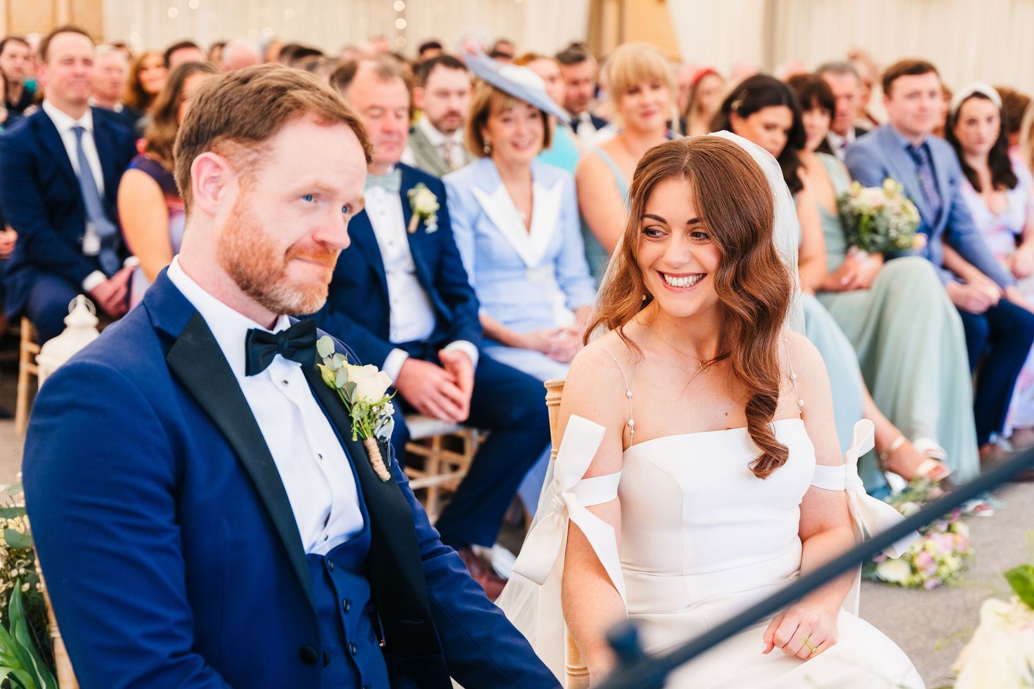 Castle Leslie Wedding Photographer Dublin Happy couple sharing joyful moment during wedding ceremony in front of seated guests.